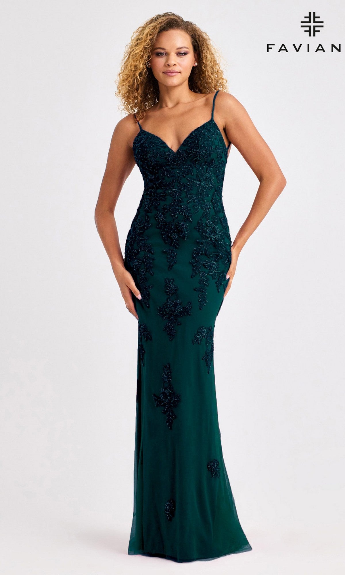 A woman in the Faviana 11428 long prom dress—dark green, floor-length, with thin straps, black lace detailing, and an open back—stands against a plain background with the FAVIAN logo in the corner.
